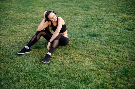 Get in shape by summer. Young active woman doing a workout in the backyard of a house. She is in sportswear and with headphones on the grass. The concept of a healthy lifestyle, self-disciplineの写真素材