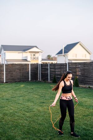 Sport lifestyle, healthy lifestyle. Cardio workout in the backyard. A young girl in sportswear is playing with a skipping rope. Weight loss workout at homeの写真素材
