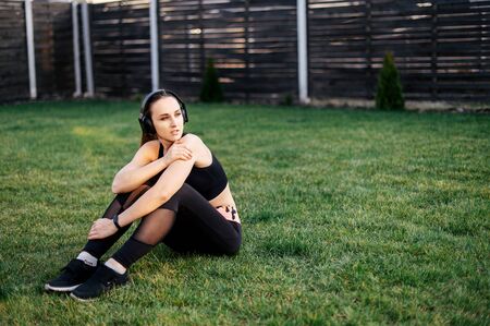 Get in shape by summer. Young active woman doing a workout in the backyard of a house. She is in sportswear and with headphones on the grass. The concept of a healthy lifestyle, self-disciplineの写真素材