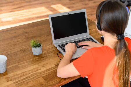 Work from home, remote work, freelance. Portrait of a young business woman working with headset for talking online and laptop at home. Back viewの写真素材