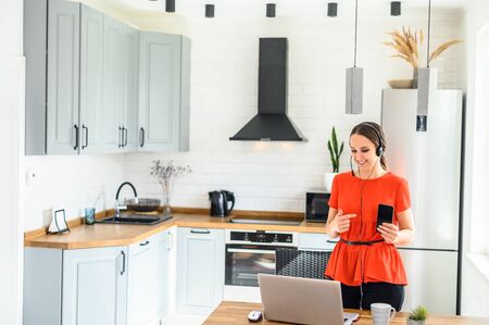 Video conference, video meeting. A young woman works from home, she uses a headset for online communication. She points finger to the phone screen. Work remotely from homeの写真素材