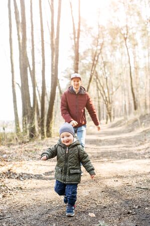 Happy childhood. Little toddler boy runs away from dad and laughs. Photo outdoors in the park in spring, autumnの写真素材