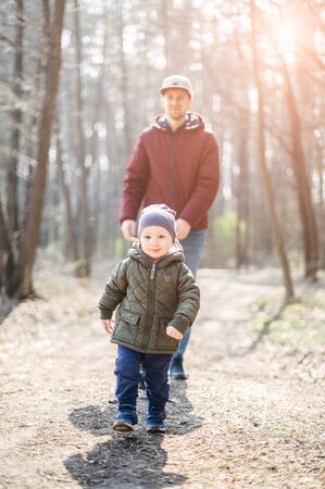 Dad and toddler outdoors together. A young father runs after the baby son, they are laughing and happy together.の写真素材