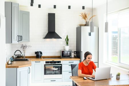Video conference from home; morning meeting remotely. A young woman uses a headset for online communication, she talk using a laptop. Work from home conceptの写真素材