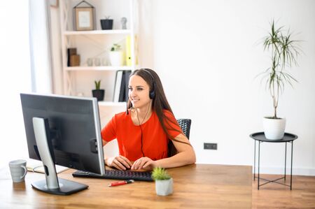 Business woman working in modern office, using headset and personal computer. She watching at screen and smiles. Concept of office workの写真素材