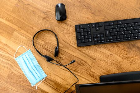 Personal computer, hands-free headset and medicine mask on the wooden table. Call centre, support during quarantine. Flat lay. Top viewの写真素材