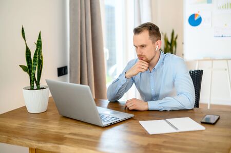 Solving business problems and tasks. Concentrated guy sits at the table with laptop, he looks at the screen with puzzled faceの写真素材