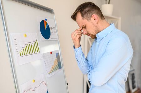Concentrated bearded guy in a formal shirt watches at a graphs and diagrams on a flipchart in a modern design office, he solves a business tasks and issues. Close up portrait. Side viewの写真素材