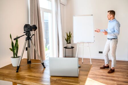 Online business coach. A young guy is recording a video on effective business management. Online Business Training. Camera on tripod and laptop on the tableの写真素材