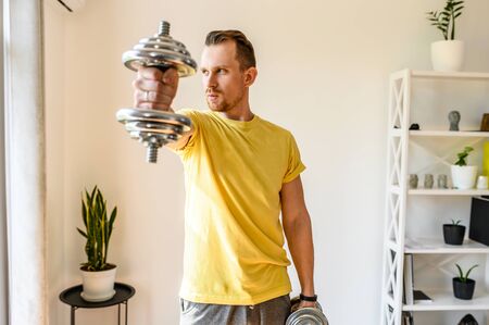 Make your shape better. Put yourself in order by the summer. The guy holds an iron dumbbell in his hand, he demonstrates it to the camera. The concept of a healthy lifestyle and strength workout at homeの写真素材