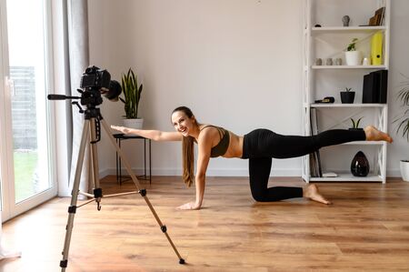 Concept of video of training, yoga video tutorial. A young woman practices yoga and records herself on camera, she in sunbird pose. Online trainer, coachの写真素材