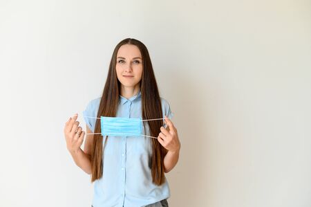 Protect yourself from a viral threat. Young woman demonstrates how to put on a medical mask on her face. Isolated picture on white backgroundの写真素材