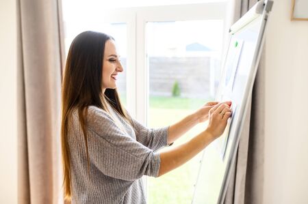 Tutor, mentor, teacher. Young positive woman hangs charts and diagrams on a flipchar board. Close up portrait, side viewの写真素材