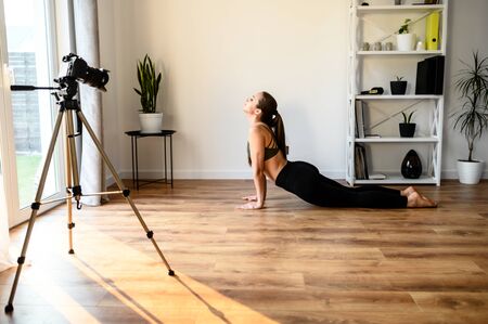 Female yoga coach at home records vlogs using camera on tripod. Concept of online learning, online classesの写真素材