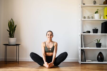 Relaxing antistress yoga at home. Young woman in a easy pose sits on the floor in sportswear barefoot. Training at homeの写真素材