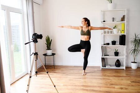 Female yoga coach at home records vlogs using camera on tripod. Concept of online learning, online classesの写真素材