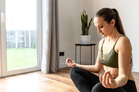 Relaxing antistress yoga at home. Young woman in a easy pose sits on the floor in sportswear barefoot. Training at homeの写真素材