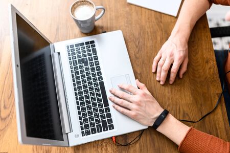 Male hands on laptop keyboard and cup of coffee on the wooden table, face is not visible. Home workplace. Flat lay. Top viewの写真素材