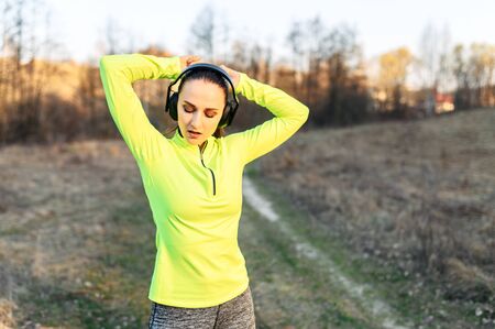 Young attractive woman in trendy sportswear with a headphones ties her hair in a bun before doing workout, she is going to run outdoors. Sport lifestyleの写真素材