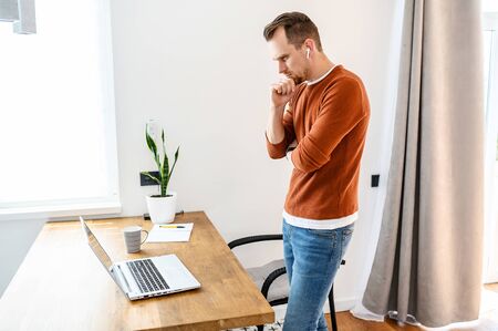 The guy uses a laptop to work. Concentrated guy looks on the screen with a serious face and thinks about something, looking for a solution to tasks. Remote workの写真素材