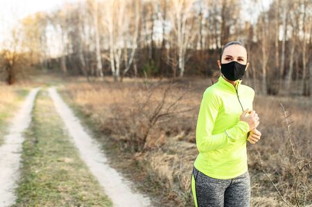 Sports during quarantine, epidemics. Young woman in a medical mask on her face jogs outdoors.の写真素材