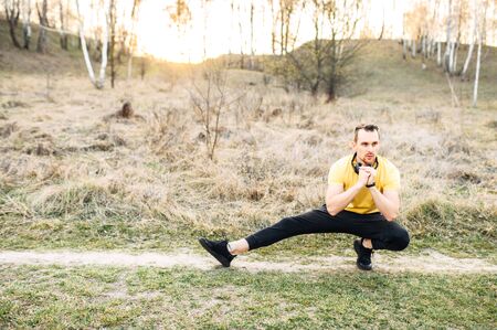 Young athletic guy with headphones is doing workout outdoors. He warm up before load. The concept of self-discipline and a healthy lifestyle.の写真素材