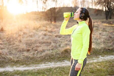 Restoring the body's water balance during sports. Young woman in sportswear outdoors drinks water from a sports bottleの写真素材