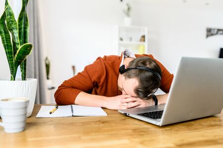 Fatigue from work. The guy with the hands-free headset rested his head in his hands, he was asleep in the workplace in front of the laptopの写真素材