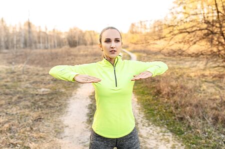 Healthy lifestyle concept. Young fit girl in sportswear doing warm-up, stretching in the countrysideの写真素材
