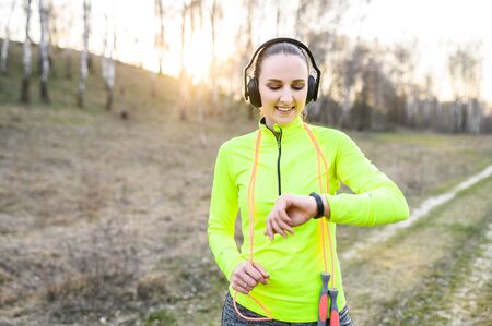 Pulse control and lose calories control with fitness tracker. A young woman has outdoors workout, she looks at fitness tracker bracelet with a smile. She satisfied with resultsの写真素材