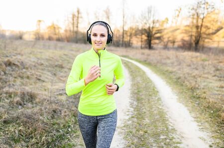 Jogging in the fresh air with your favorite music. Young positive woman is running in forest, listening music in headphones and smiling.の写真素材
