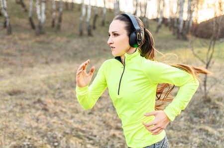 Jogging in the fresh air with your favorite music. Young positive woman is running in forest, listening music in headphonesの写真素材