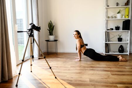 Concept of video of training, yoga video tutorial. A young woman practices yoga and records herself on camera. Online trainer, coachの写真素材