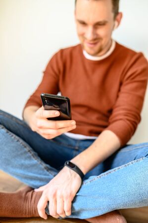 Smartphone in the hands of a guy close-up. The guy looks at the screen and smiles, he is out of focusの写真素材