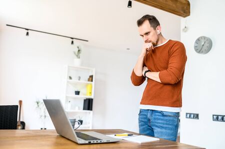 The guy uses a laptop to work. Concentrated guy looks on the screen with a serious face and thinks about something, looking for a solution to tasks. Remote workの写真素材
