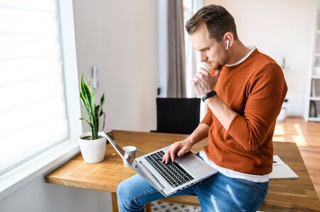 The guy uses a laptop to work. Concentrated guy looks on the screen with a serious face and thinks about something, looking for a solution to tasks. Remote workの写真素材