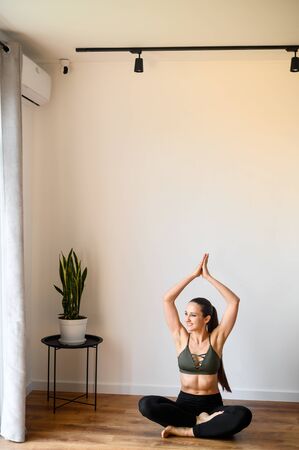 Relaxing antistress yoga at home. Young woman in a easy pose sits on the floor in sportswear barefoot. Training at homeの写真素材