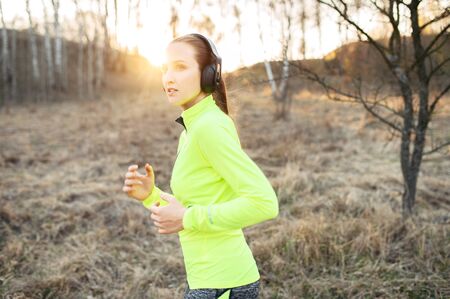 Close-up portrait of young attractive woman in trendy sportswear with a headphones, she runs, jogging outdoors. Sport lifestyleの写真素材