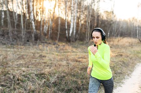 Sports lifestyle. Young woman in bright sportswear with earphones runs outdoorsの写真素材