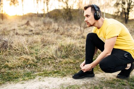 Athletic guy with headphones tied shoelaces and is going to jog in the forest. Healthy lifestyle conceptの写真素材