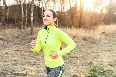 Doing sports outdoors. Young slim woman in neon sportswear jogging in the countrysideの写真素材