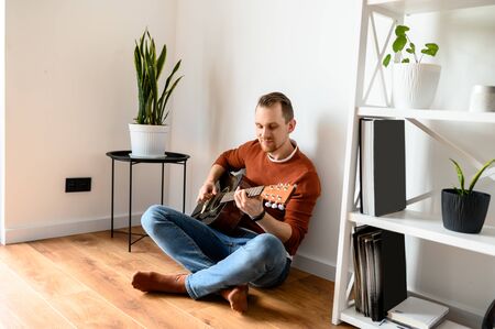 Home leisure. A young guy plays acoustic guitar in the living roomの写真素材