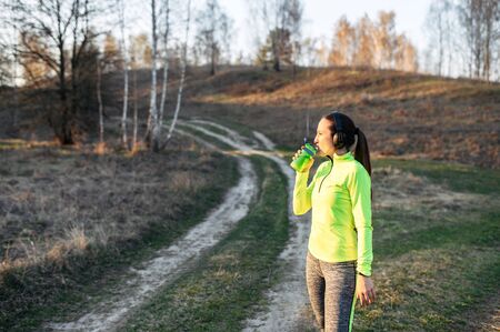 Restoring the body's water balance during sports. Young woman in sportswear outdoors drinks water from a sports bottleの写真素材
