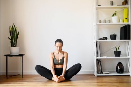 Relaxing antistress yoga at home. Young woman in a easy pose sits on the floor in sportswear barefoot. Training at homeの写真素材