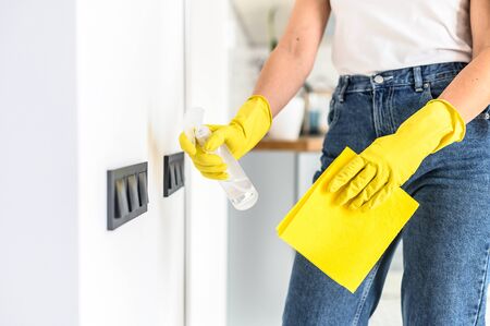 Close-up picture of hands in yellow protective rubber gloves is spraying disinfectant on the wall...