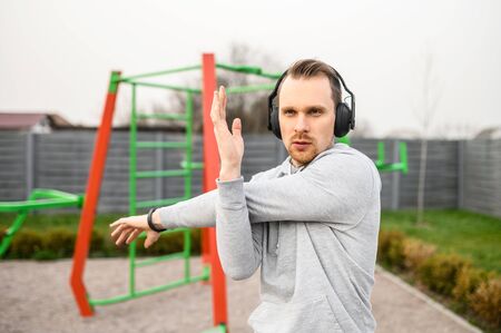 Athletic guy in a hoodie does upper body stretching and warming up before a workout outdoors....