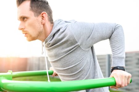 Outdoors workout. An athletic guy is doing triceps dips on parallel bars. Healthy lifestyle concept