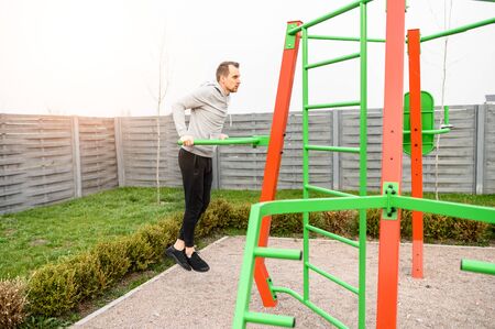 Athletic young man is doing exercises on parallel bars outdoors. Healthy lifestyle concept