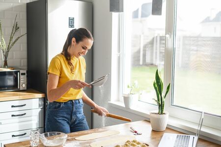 Learn cooking online. A young woman is watching cooking tutorial video in the kitchen and sift a flour, she is going to bakeの写真素材