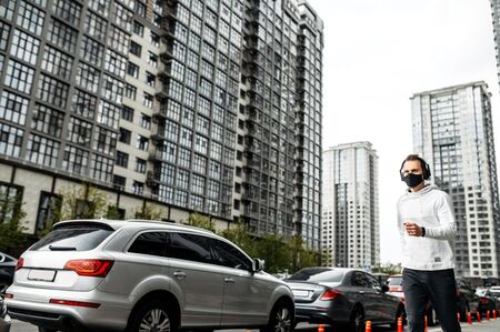 Keep fit during quarantine. A young guy runs in a mask in a cityscape, high-rise buildings on the...